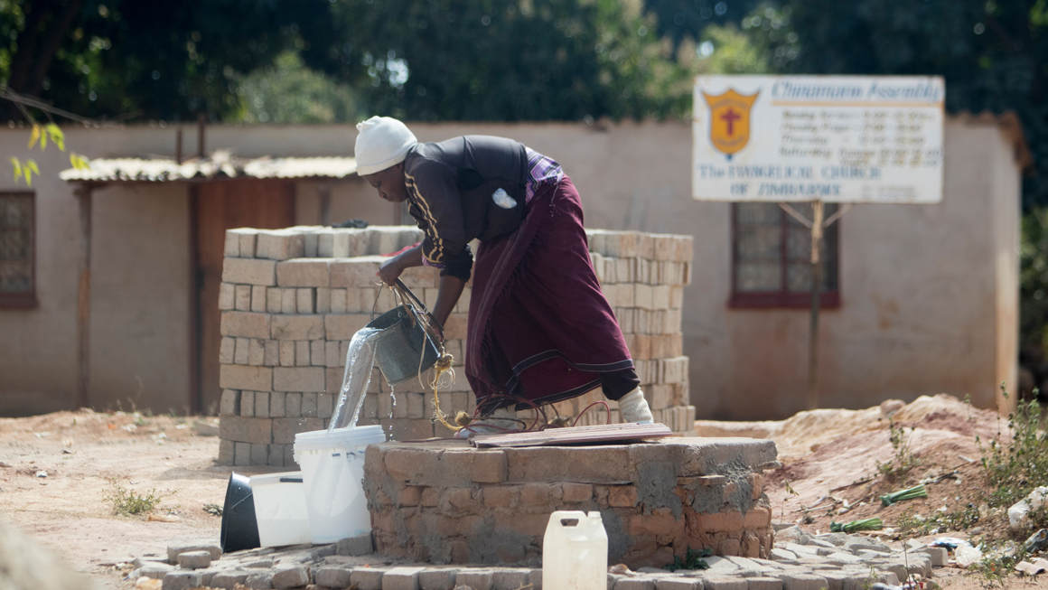 A woman collects water from a community well in Epworth. Image by Wifred Kajese
